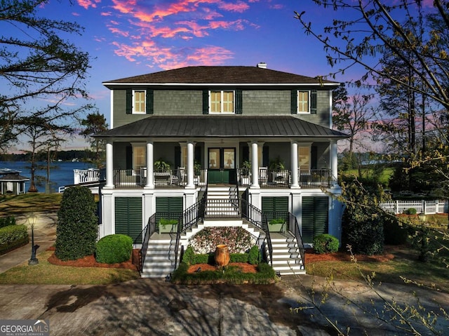 view of front facade featuring metal roof, a water view, stairs, a standing seam roof, and a porch