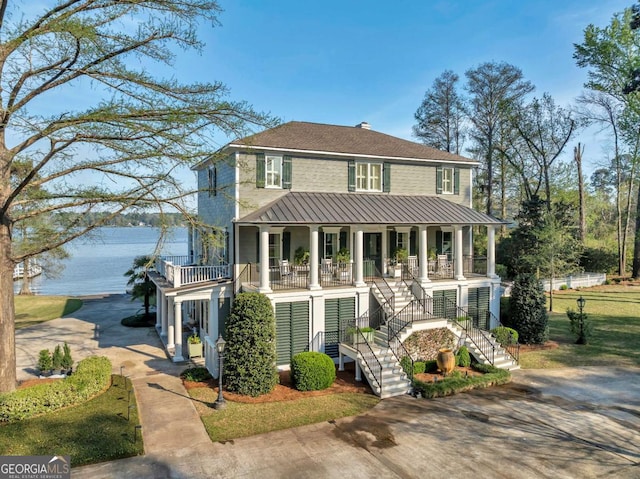 view of front of house featuring a water view, stairway, driveway, covered porch, and a shingled roof