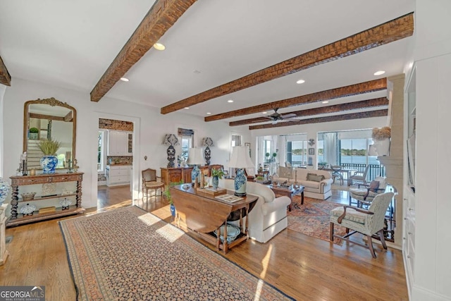 living room with a ceiling fan, beamed ceiling, and wood finished floors
