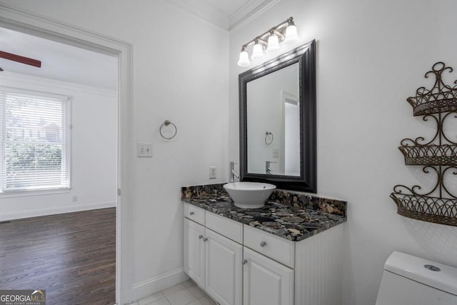 half bath with vanity, crown molding, toilet, baseboards, and wood finished floors