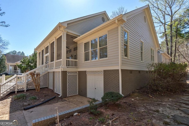 rear view of house with an attached garage, a sunroom, brick siding, and stairway