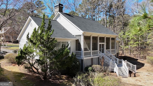 view of side of property featuring a sunroom, a chimney, stairs, and roof with shingles
