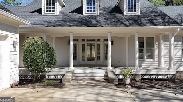 view of exterior entry featuring covered porch and roof with shingles