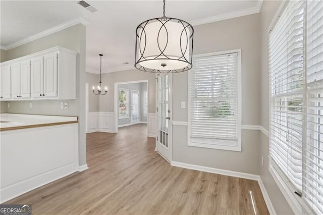 unfurnished dining area featuring a wainscoted wall, visible vents, ornamental molding, light wood-style floors, and a notable chandelier