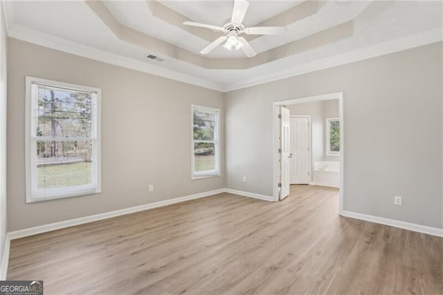 spare room featuring light wood finished floors, a raised ceiling, visible vents, crown molding, and ceiling fan