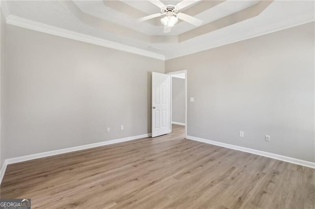 empty room with a tray ceiling, light wood-type flooring, baseboards, ceiling fan, and crown molding