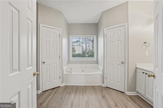 bathroom featuring baseboards, wood finished floors, a garden tub, and vanity