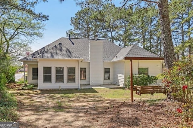 rear view of property featuring a patio, a shingled roof, and a chimney