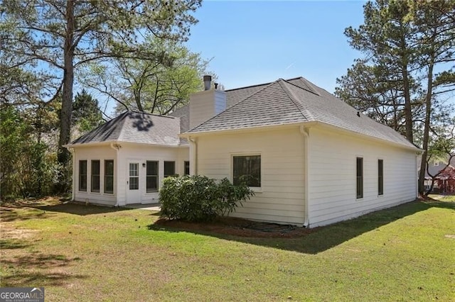 back of property with a chimney, roof with shingles, and a yard