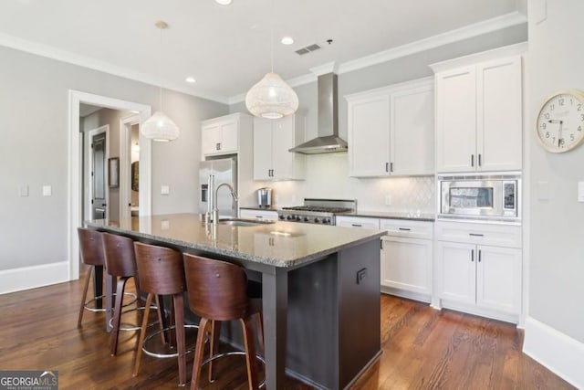 kitchen with wall chimney exhaust hood, stainless steel appliances, a kitchen island with sink, a sink, and white cabinetry