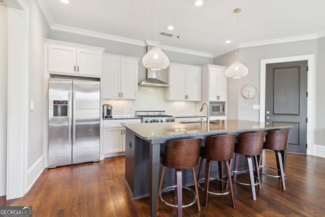 kitchen featuring stainless steel appliances, a sink, white cabinetry, ornamental molding, and a center island with sink