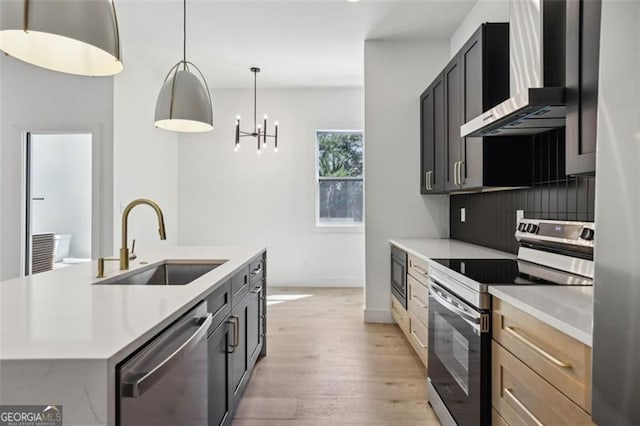 kitchen featuring wall chimney range hood, light countertops, a sink, and stainless steel appliances