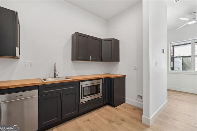kitchen with a sink, butcher block countertops, appliances with stainless steel finishes, baseboards, and light wood-style floors