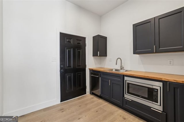 kitchen featuring stainless steel microwave, a sink, wood counters, dishwasher, and light wood-style flooring