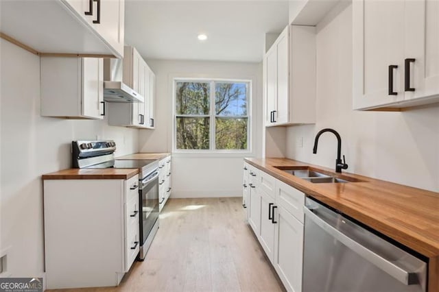 kitchen featuring wooden counters, appliances with stainless steel finishes, white cabinetry, a sink, and light wood-style floors