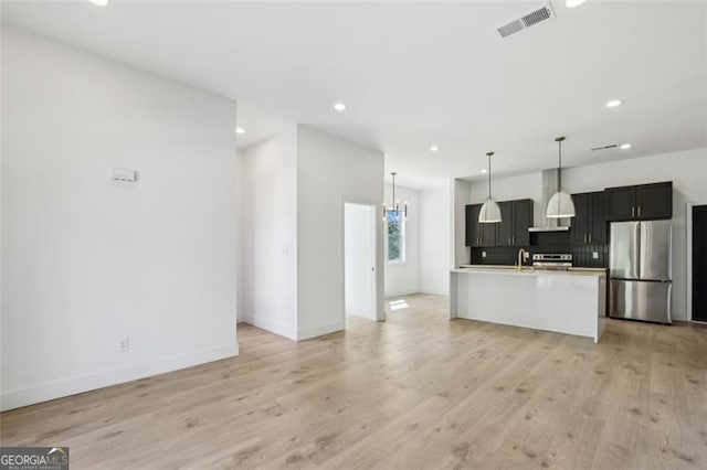 kitchen featuring light countertops, tasteful backsplash, light wood finished floors, visible vents, and freestanding refrigerator