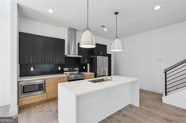 kitchen featuring light countertops, a sink, stainless steel appliances, wall chimney range hood, and decorative backsplash