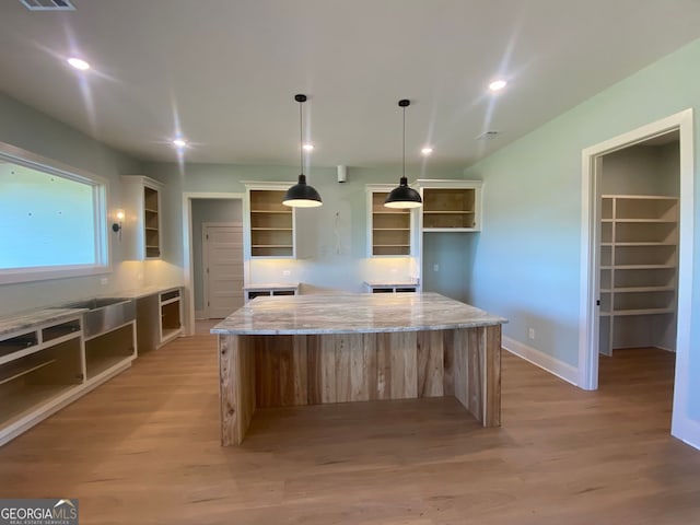 kitchen with open shelves, a spacious island, light wood finished floors, and light stone countertops
