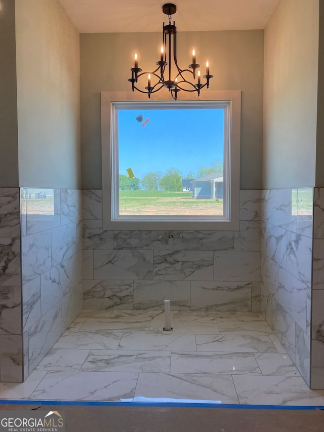bathroom featuring an inviting chandelier, marble finish floor, a wainscoted wall, and tile walls