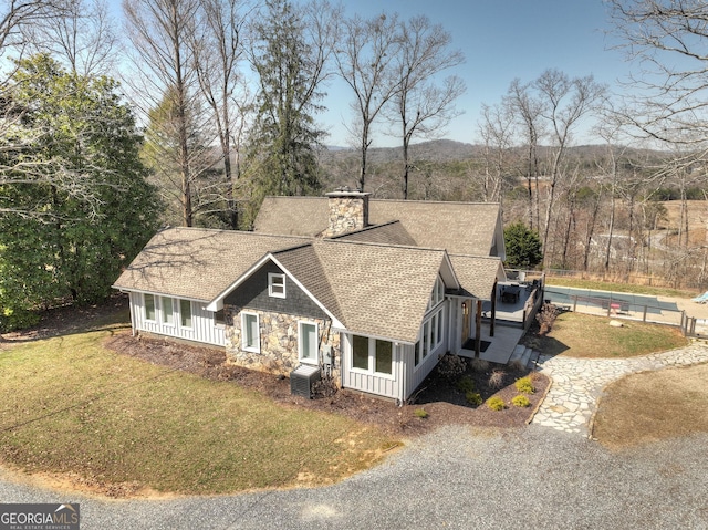 view of front of house featuring stone siding, a chimney, a front lawn, and roof with shingles