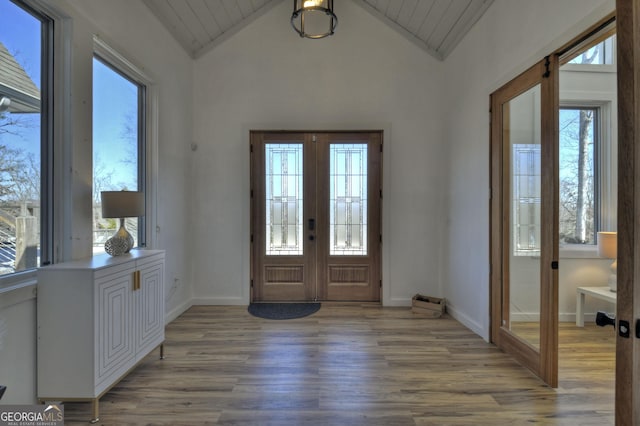 foyer featuring baseboards, vaulted ceiling, light wood-style flooring, and french doors
