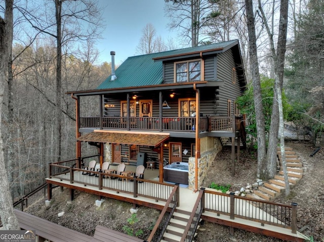 rear view of property with stairway, a wooden deck, log exterior, a hot tub, and metal roof