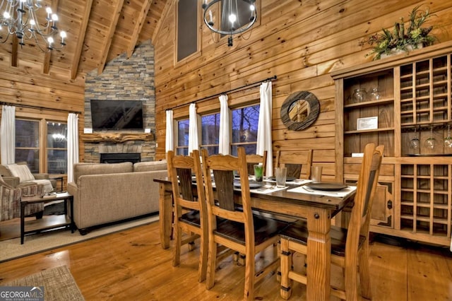 dining room with a stone fireplace, beam ceiling, hardwood / wood-style floors, an inviting chandelier, and wood ceiling