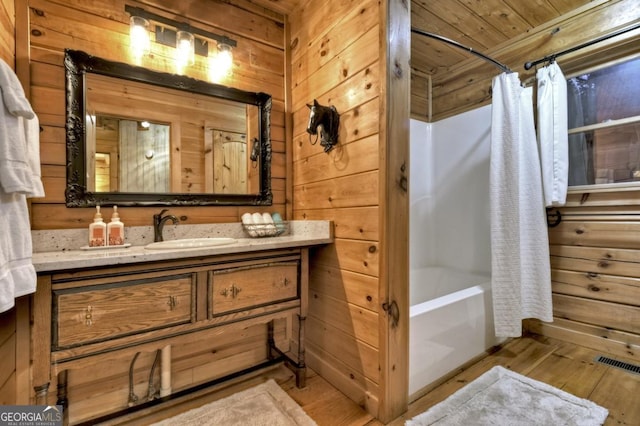 full bath featuring shower / bath combo, visible vents, wood walls, wood finished floors, and vanity