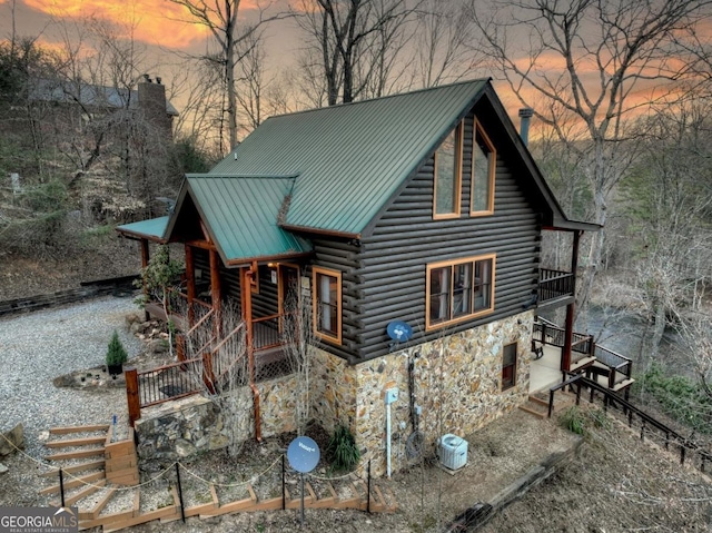 view of front facade featuring stone siding, log exterior, stairs, and metal roof