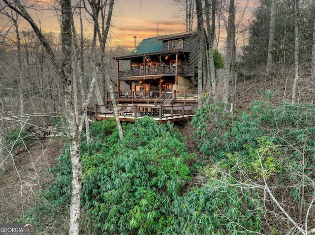 back of property at dusk featuring a balcony and a forest view