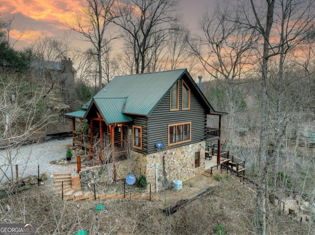 view of front facade featuring stone siding, metal roof, central air condition unit, log exterior, and a chimney