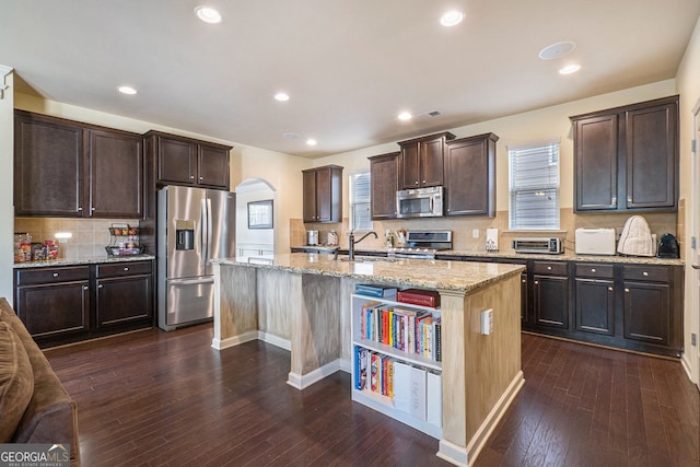 307 Montgomery Way, Woodstock, GA 30188 - kitchen featuring appliances with stainless steel finishes, arched walkways, dark brown cabinetry, backsplash, and an island with sink