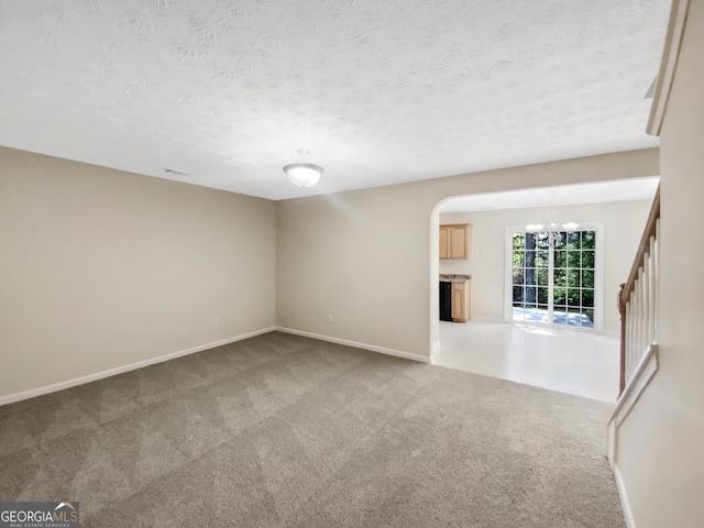 1005 Magnolia Gardens Walk, Mcdonough, GA 30253 - spare room featuring a textured ceiling, baseboards, arched walkways, a notable chandelier, and light colored carpet