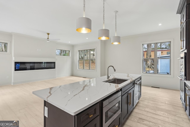 kitchen featuring a sink, a ceiling fan, a glass covered fireplace, stainless steel appliances, and light wood-style floors