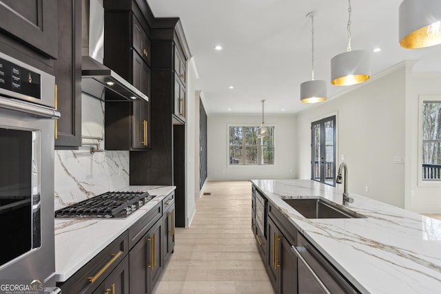 kitchen featuring decorative backsplash, stainless steel appliances, a sink, pendant lighting, and wall chimney range hood