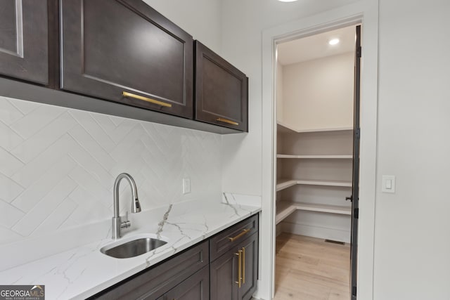 interior space featuring decorative backsplash, light stone countertops, dark brown cabinetry, a sink, and light wood-type flooring
