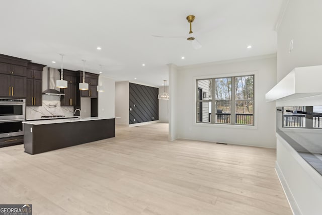 kitchen with light countertops, dark brown cabinetry, open floor plan, wall chimney range hood, and backsplash