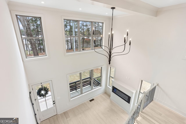 interior space with visible vents, baseboards, light wood-type flooring, a glass covered fireplace, and an inviting chandelier