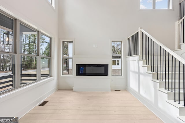 unfurnished living room featuring visible vents, a high ceiling, wood finished floors, and stairway