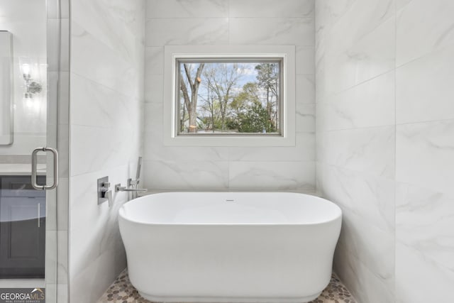 bathroom with a soaking tub, vanity, and tile walls