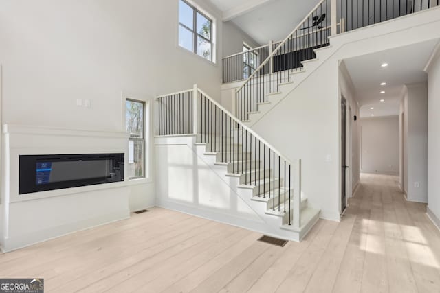 stairs featuring visible vents, wood finished floors, a towering ceiling, and a glass covered fireplace