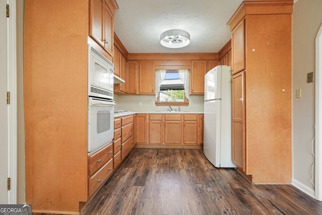 kitchen with a textured ceiling, light countertops, white appliances, dark wood finished floors, and a sink