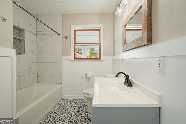 bathroom featuring vanity, toilet, a textured ceiling, washtub / shower combination, and wainscoting