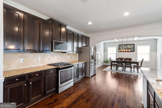 kitchen featuring dark brown cabinets, light stone countertops, decorative backsplash, stainless steel appliances, and arched walkways