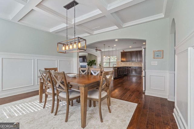 dining room featuring a ceiling fan, arched walkways, a decorative wall, and dark wood-style floors