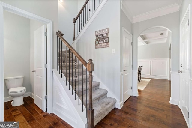 stairway featuring arched walkways, hardwood / wood-style flooring, crown molding, and beam ceiling