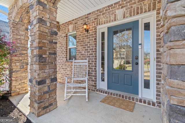 doorway to property featuring brick siding and a porch