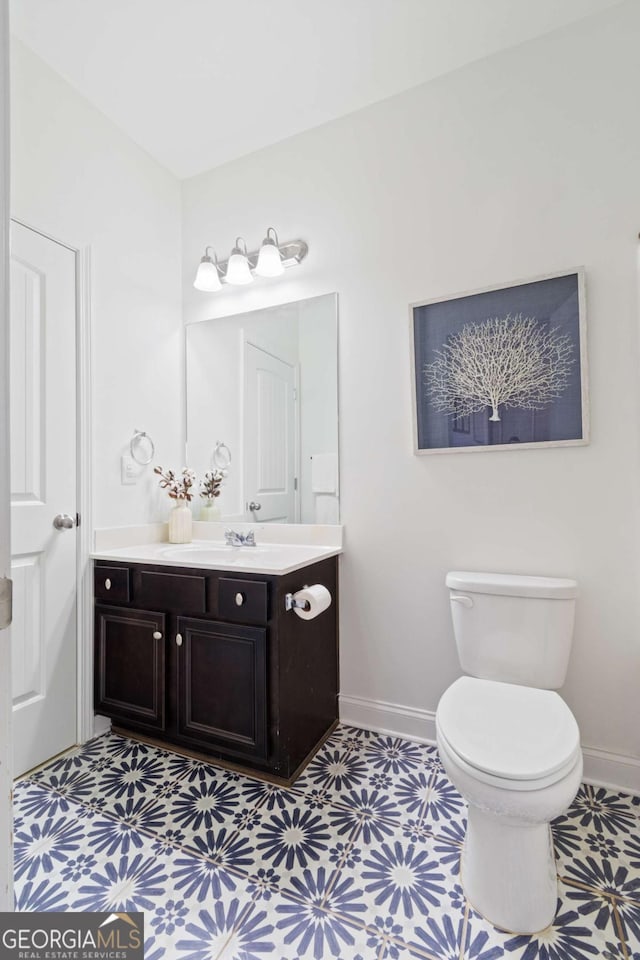 half bathroom featuring tile patterned floors, vanity, baseboards, and toilet