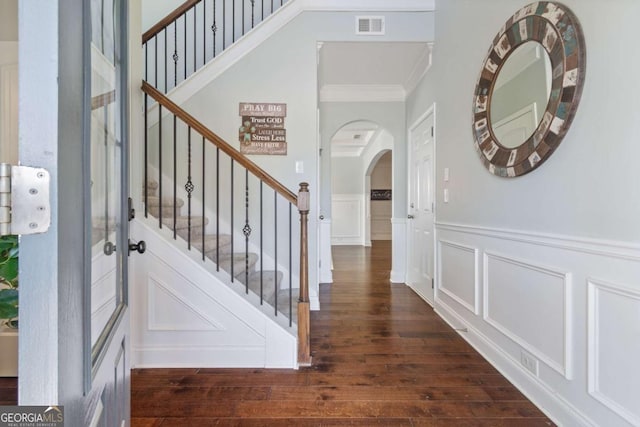 staircase featuring crown molding, visible vents, hardwood / wood-style floors, a decorative wall, and arched walkways