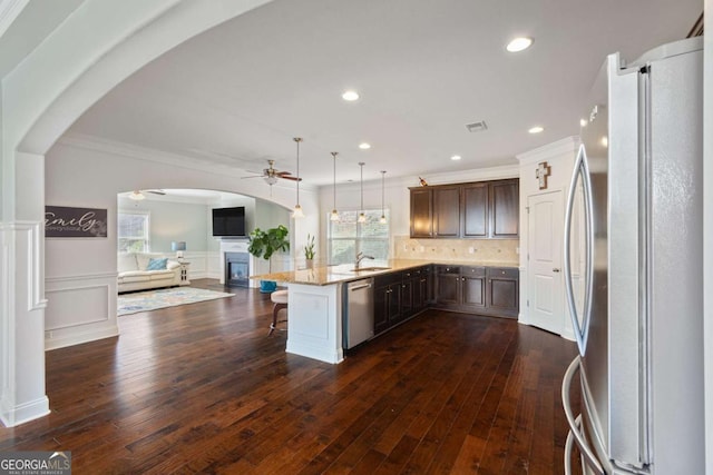 kitchen with arched walkways, open floor plan, a ceiling fan, crown molding, and stainless steel appliances